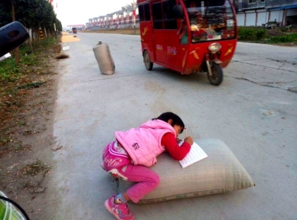 下午放学后,一名留守儿童趴在粮食包上写家庭作业。
