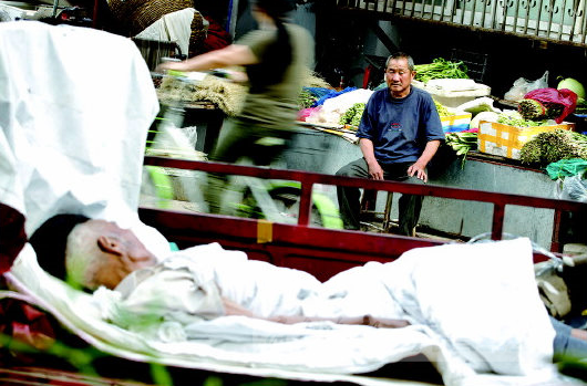 老柴将躺在三轮车里的父亲安置在摊位对面的拐角处,随时关注他的一举一动。 王鑫 摄