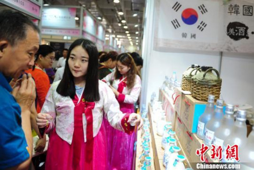 2016第五届(济南)韩国商品博览会1日在济南举行，身穿韩国民族服饰的展商向采购商介绍韩国酒。　张勇 摄