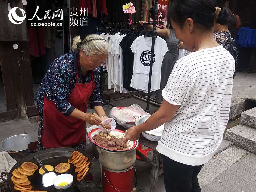 图为游客向徐业梅卖当地小吃。王钦摄