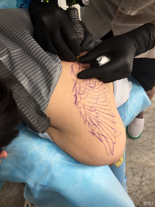 在刺青店内的床上,让刺青师傅在自己的肩膀处纹上一组紫色花纹的纹身